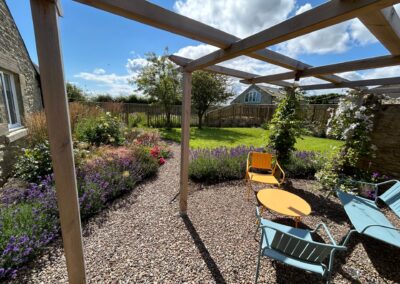 A picturesque garden featuring wildflowers, lush green turf, and a seating area with pastel-coloured chairs.